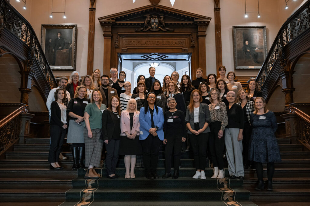 A group of breast cancer advocates stand together on a staircase in a government building